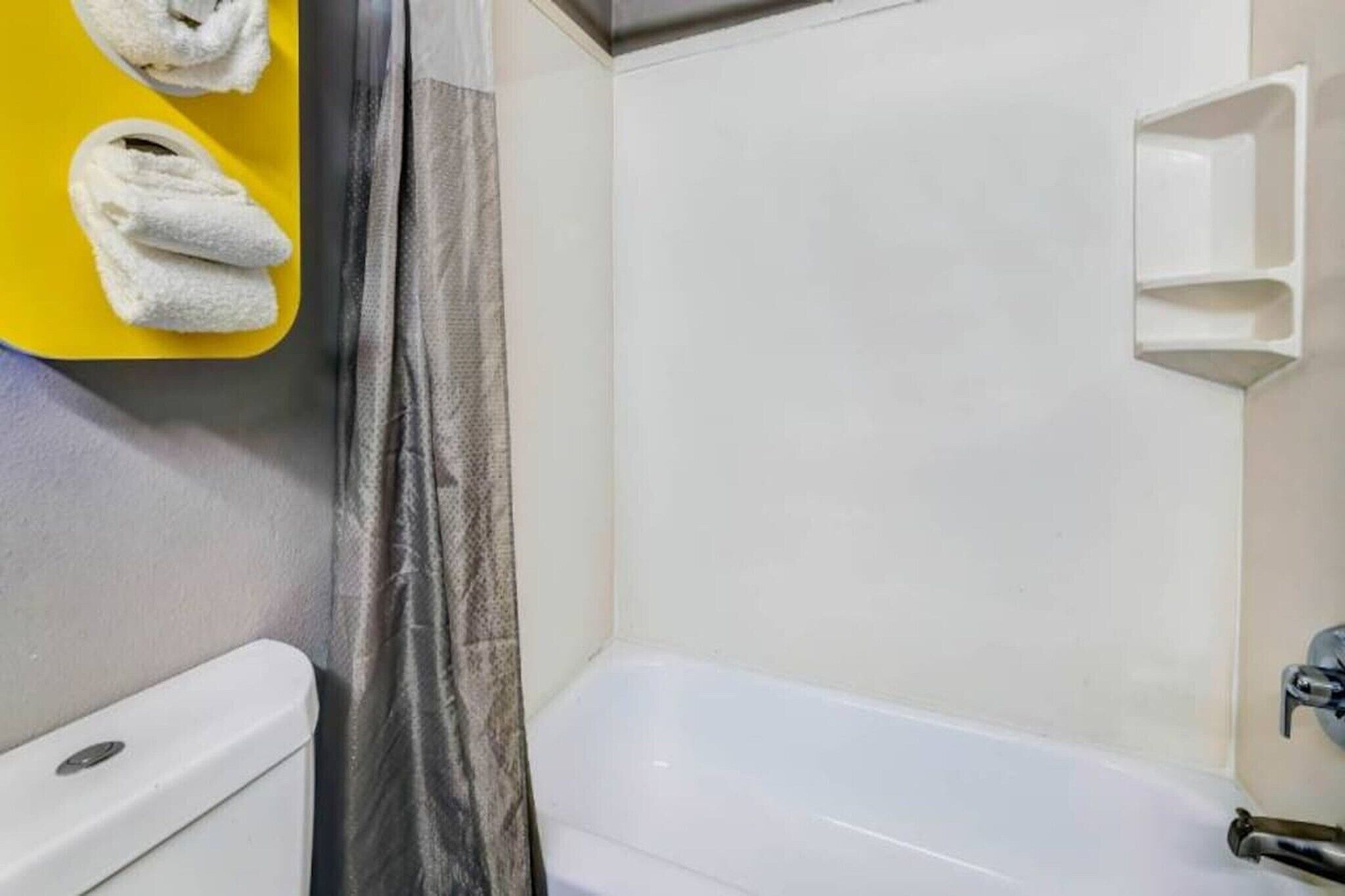 Un baño con una bañera blanca, un inodoro, una cortina de ducha y un toallero amarillo con toallas.