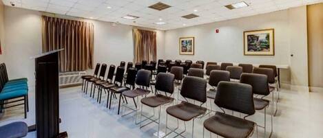 A conference room with rows of chairs, a podium, and two windows with curtains.