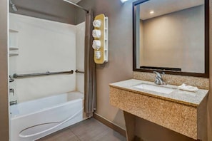 Ein Badezimmer mit einer Badewanne, einem Waschbecken mit Granitplatte, einem Handtuchhalter und einem Spiegel.