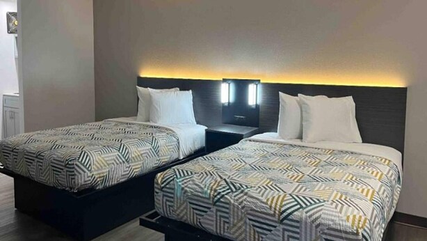 Two beds with patterned bedding, a nightstand, and a wall-mounted light fixture.