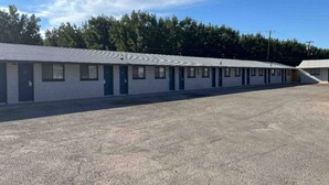A motel with a row of rooms, a parking lot, and a forested area in the background.
