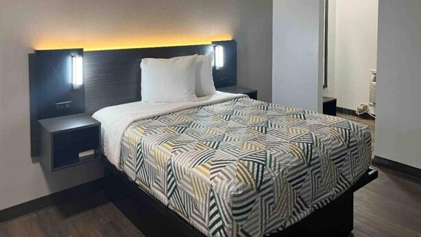 A hotel room with a bed, nightstands, a headboard with integrated lighting, and a visible door.