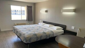 A hotel room with a bed, a desk, a chair, a window with curtains, and a wall-mounted light fixture. - 1 King Bed | Mobility Accessible Tub, Nsmk (Wichita Falls TX)
