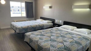 A hotel room with two beds, a window with curtains, wall-mounted light fixtures, and a view of a building outside. - 2 Queen Beds | Mobility Accessible Tub Nsmk (Wichita Falls)