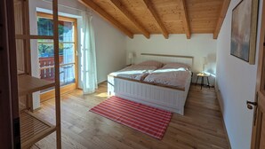 A bedroom with a wooden ceiling, a bed with white headboard, a red and white striped rug, and a view of the outdoors through a glass door. - Apartment Gigi 100 m², 2-6 persons, living room, 3 bedrooms, kitchen, 2x bathroom, WLAN (Unterwössen)