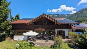 A wooden house with a sloped roof, solar panels, and a patio with outdoor furniture. - Apartment Gigi 100 m², 2-6 persons, living room, 3 bedrooms, kitchen, 2x bathroom, WLAN (Unterwössen)