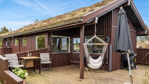 En stuga av trä med en veranda, en hängstol och ett bord med stolar.