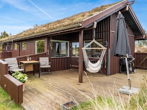 A wooden cabin with a deck, a hanging chair, and a table with chairs. - "Thorgny" - 1km from the sea by Interhome (Pandrup)