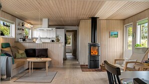 En mysig stuga med trägolv, en soffa, ett matbord, en öppen spis och ett köksutrymme.