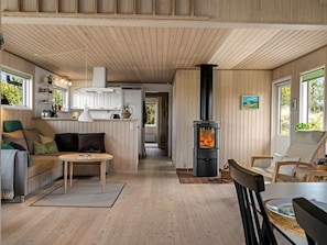 A cozy cabin interior with a wooden floor, a sofa, a dining table, a fireplace, and a kitchen area. - "Thorgny" - 1km from the sea by Interhome (Pandrup)