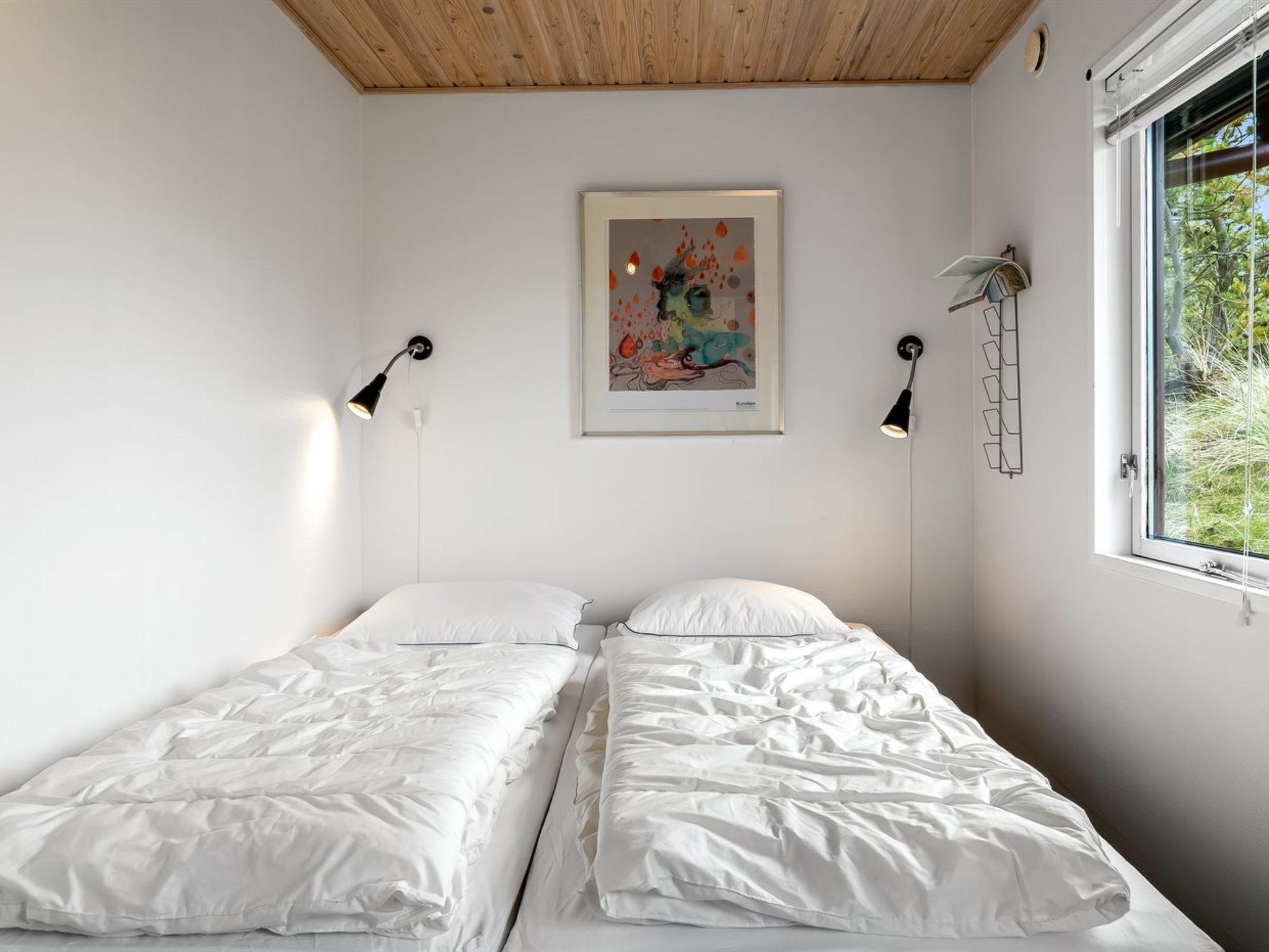 Une chambre avec deux lits simples, un plafond en bois, une œuvre d’art encadrée et une fenêtre donnant sur un paysage verdoyant.