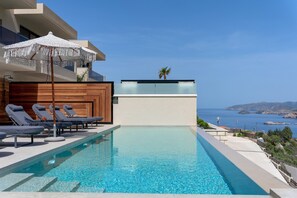 Ein Swimmingpool mit Liegestühlen, einer Holzterrasse und Blick auf das Meer.