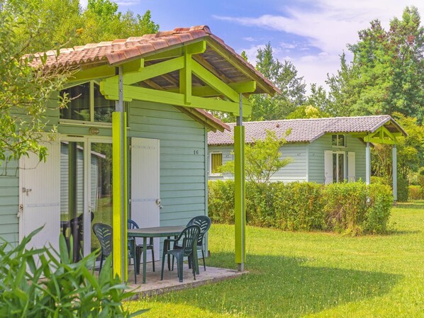 Un edificio con techo verde, un patio y sillas, rodeado de vegetación.
