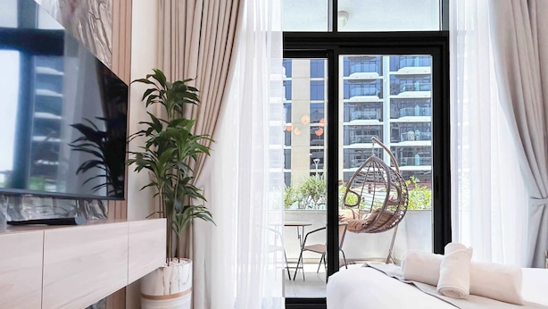Une chambre d’hôtel moderne équipée d’un lit, d’une télévision, d’une plante en pot et d’un balcon agrémenté d’un fauteuil suspendu.