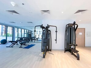 Ein moderner Fitnessraum mit Trainingsgeräten, großen Fenstern und Holzboden.