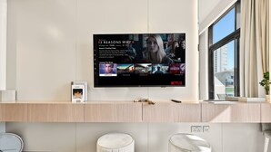Un soggiorno moderno con una televisione a schermo piatto che mostra l'interfaccia di Netflix, un mobiletto basso in legno chiaro e un'ampia finestra.