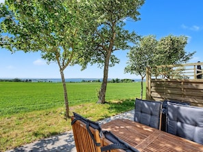 Une table en bois avec des coussins, une vue sur un champ verdoyant et des arbres.