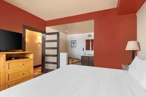 Ein Hotelzimmer mit Bett, Holzkommode, Fernseher und einer kleinen Küchenzeile.