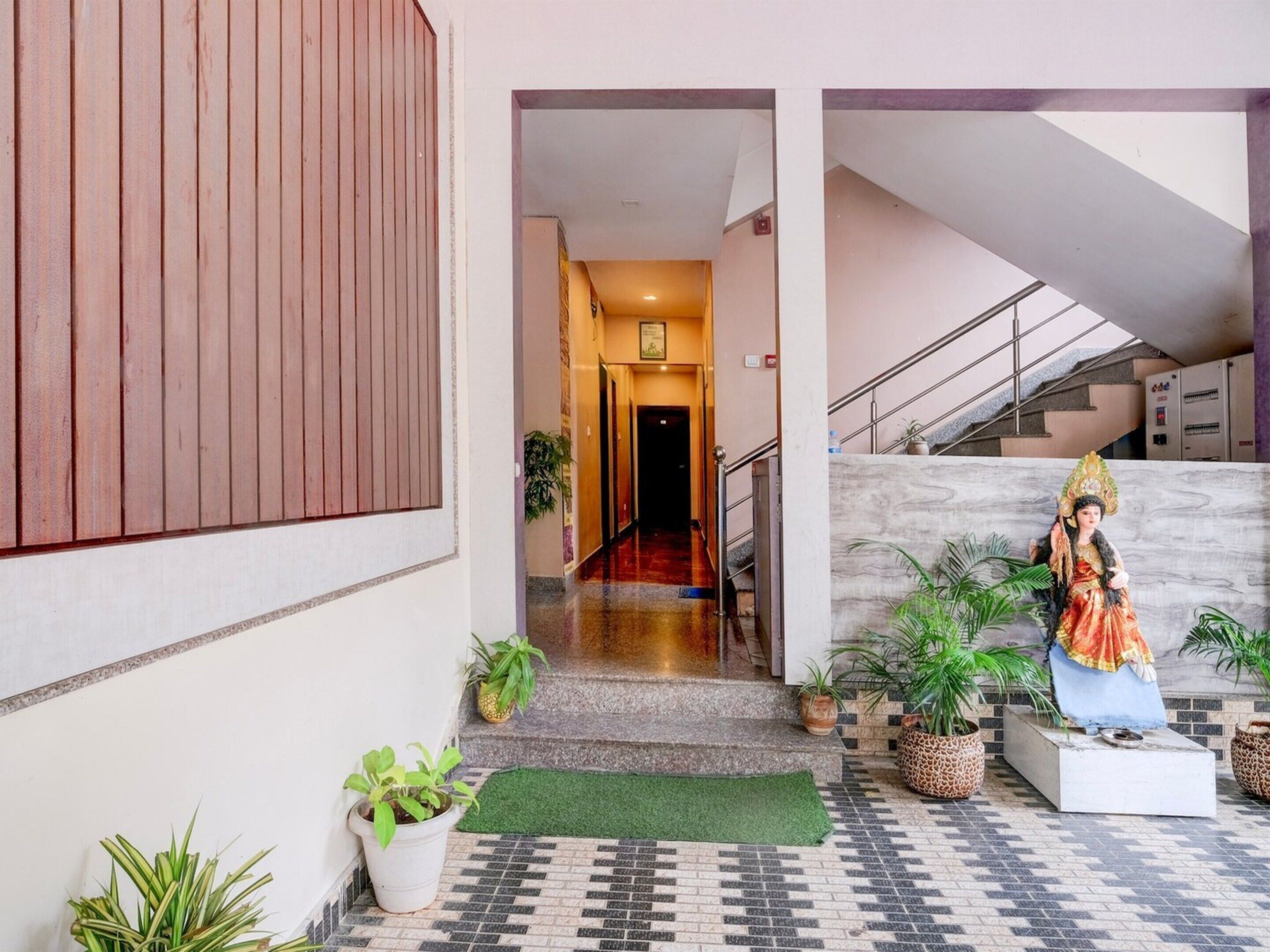 Entrada de hotel com uma escadaria de mármore, uma estátua, plantas em vasos e piso de azulejos.