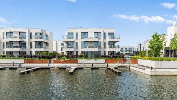 A modern building with balconies, a water feature in front, and a clear sky. - Sol Marina- Przystań by Grand Apartments (Pruszcz Gdanski)