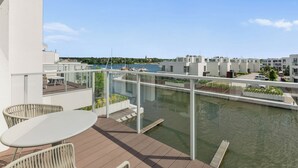 A modern balcony with a glass railing overlooking a body of water, a small table, and wicker chairs. - Sol Marina- Przystań by Grand Apartments (Pruszcz Gdanski)