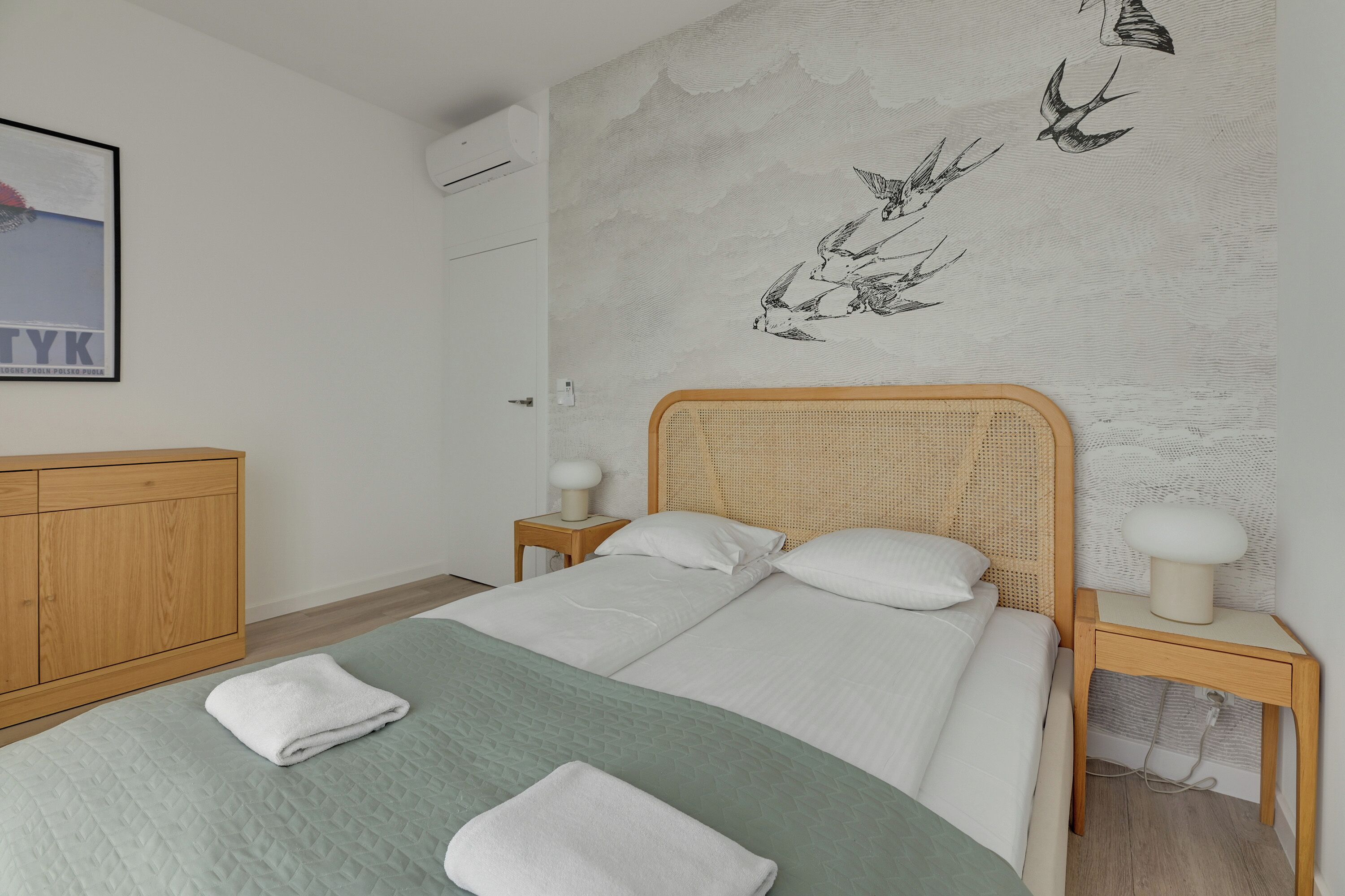 Un dormitorio con cama, dos mesitas de noche, un armario de madera y una pared decorada con un mural de aves.
