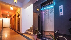 A hotel corridor with a staircase leading to an elevator, potted plants, and a wall-mounted intercom. - Hotel Aurang Heritage (Jaisalmer)