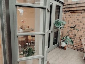 Une vĂ©randa dotĂ©e dâune porte en verre, dâun mur en briques et de plantes en pot.