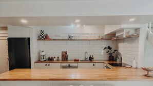 Une cuisine moderne avec un plan de travail en bois, des armoires blanches, un réfrigérateur noir et un petit îlot central agrémenté de deux chaises à rayures.