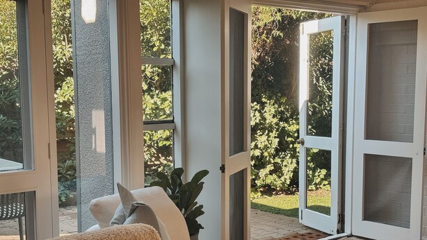 Un salon avec un canapé, une table basse et une vue sur un jardin, accessible par de grandes portes vitrées.