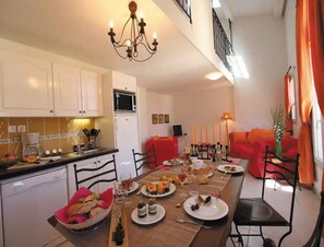 A dining area with a table set for a meal, a kitchen with white cabinets, a microwave, and a coffee maker. - Duplex Apartment Near Maussane-les-alpilles (Paradou)