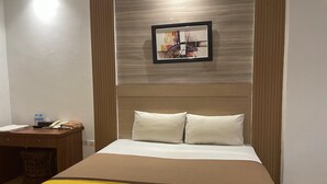 Una habitación de hotel con una cama, un escritorio, una silla, un cuadro en la pared y una ventana.