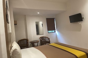 A hotel room with a bed, two chairs, a small table, a television, and a window with a blind.