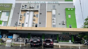 Un hotel con fachada moderna, varios equipos de aire acondicionado y un estacionamiento con dos coches.