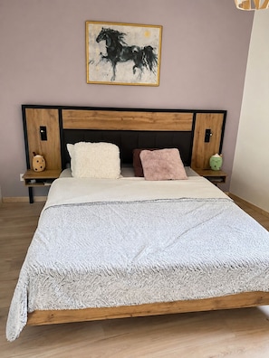 A bedroom with a wooden headboard, a bed with a textured white blanket, two pillows, a wall-mounted painting of a horse, and bedside tables with decorative items. - L'élixir, a cozy bed-and-breakfast in Ardèche, surrounded by nature, where you can bring your dog (Sécheras)