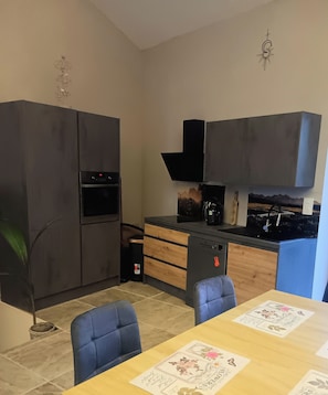A compact kitchen with a built-in oven, a coffee machine, and a dining area with a table and chairs. - L'élixir, a cozy bed-and-breakfast in Ardèche, surrounded by nature, where you can bring your dog (Sécheras)