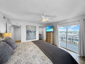 A bedroom with a bed, a ceiling fan, a TV, a painting, and a balcony with a view. - Ocean House 2701 Beachfront (Gulf Shores)