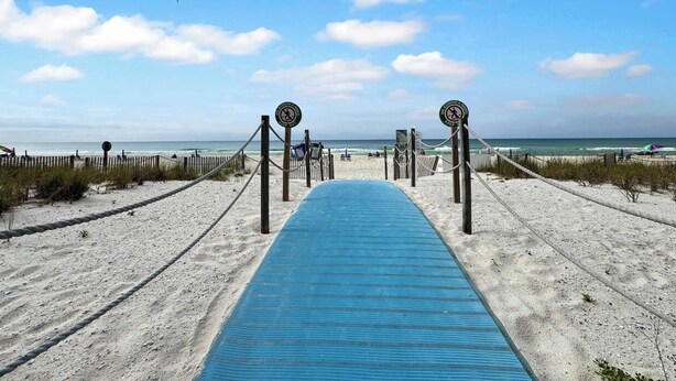 Ein Strandweg führt zum Meer, mit einer blauen Matte, Holzpfählen und Schildern.
