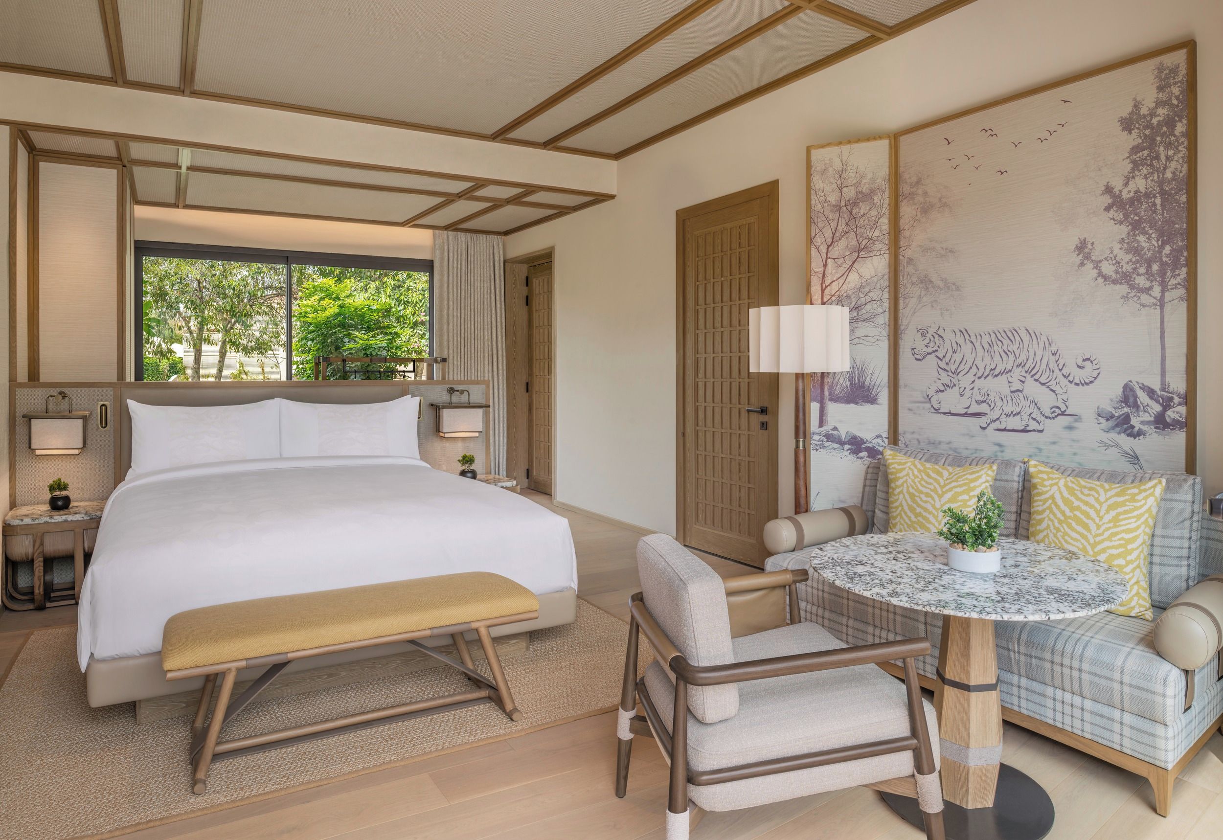 A spacious bedroom with a large bed, bedside tables, a bench, a sofa, and a small round table.