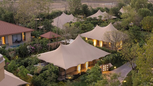 A series of tent-like structures with a pool and lush greenery in the background. - JW Marriott Ranthambore Resort & Spa (Sawai Madhopur)
