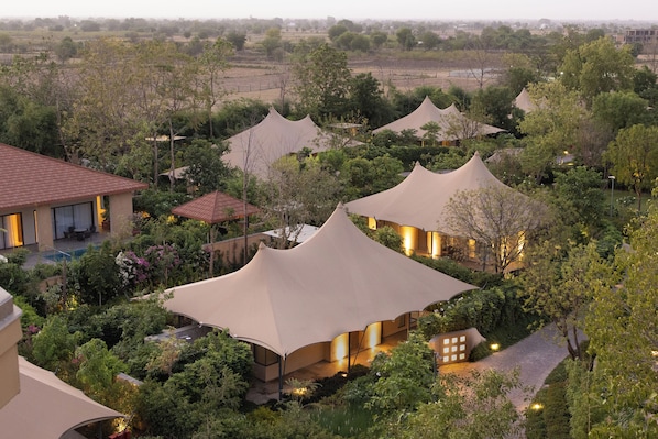 A series of tent-like structures with a pool and lush greenery in the background.