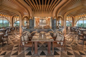 Un vaste espace de salle à manger avec un îlot central, de hauts plafonds avec des poutres en bois et une vue sur l’extérieur grâce à de grandes fenêtres.