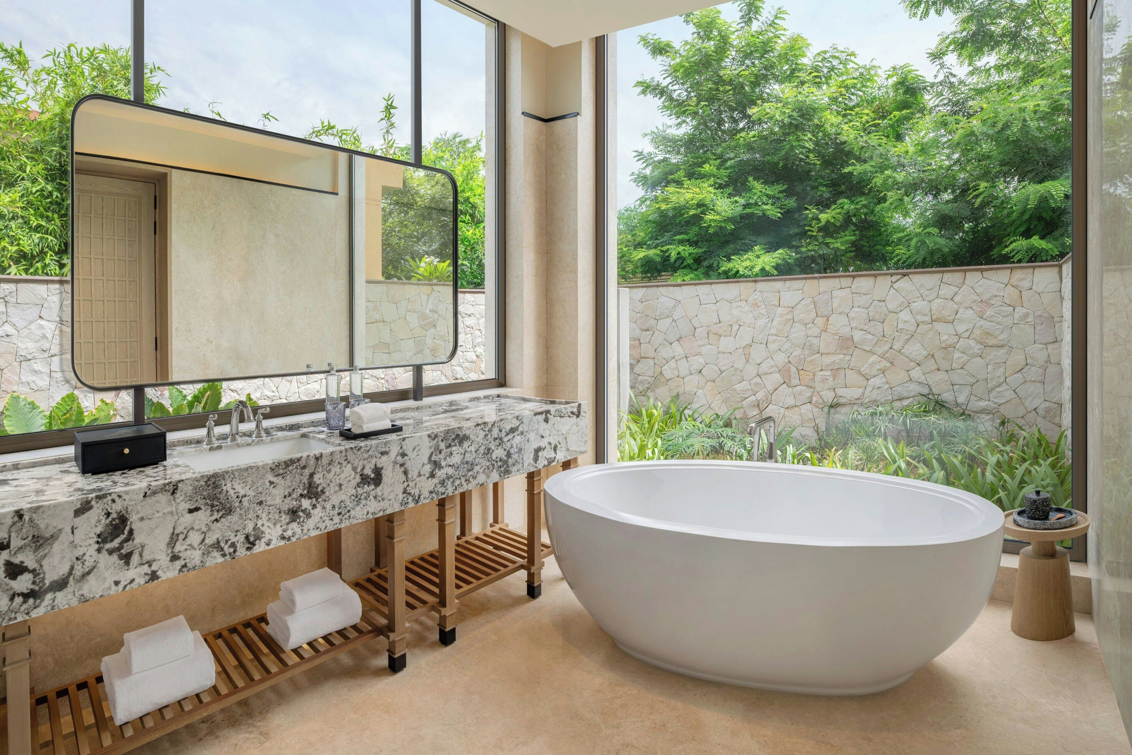 Un baño moderno con una bañera independiente, un espejo grande y vistas a zonas verdes.