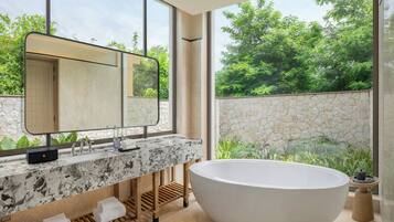 Un baño moderno con una bañera independiente, un espejo grande y vistas a zonas verdes.