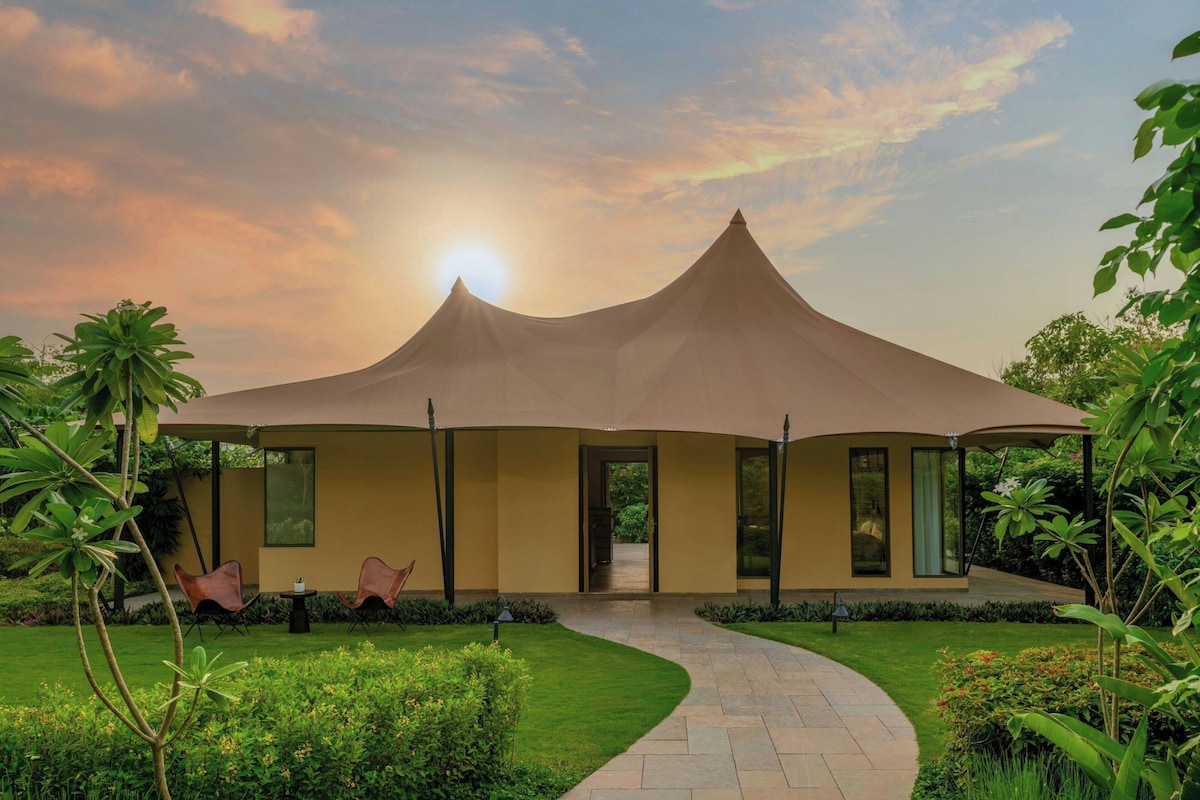 A modern building with a unique conical roof structure, surrounded by lush greenery and a well-maintained garden.