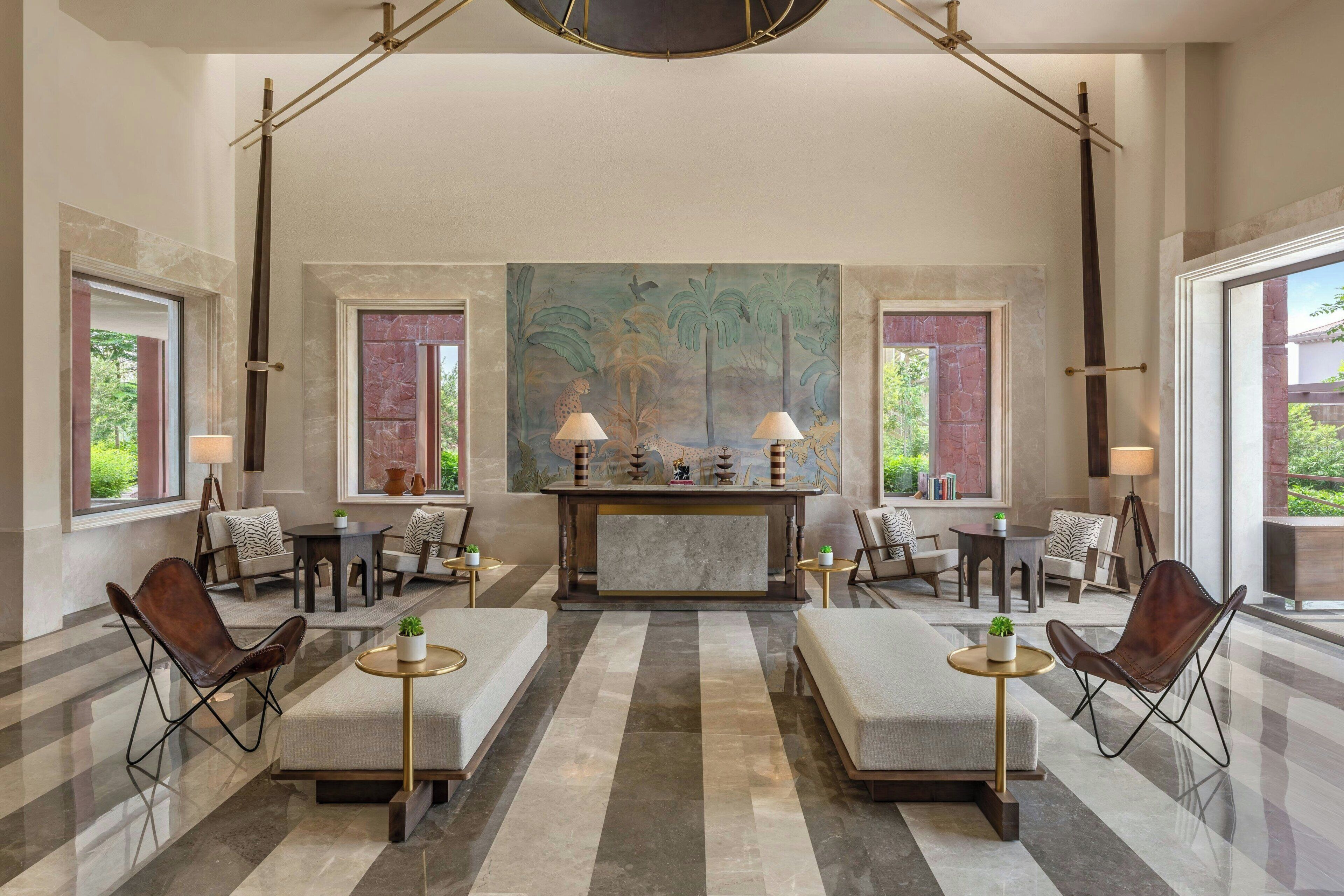 A lobby with a reception desk, seating arrangements, and a large painting on the wall.