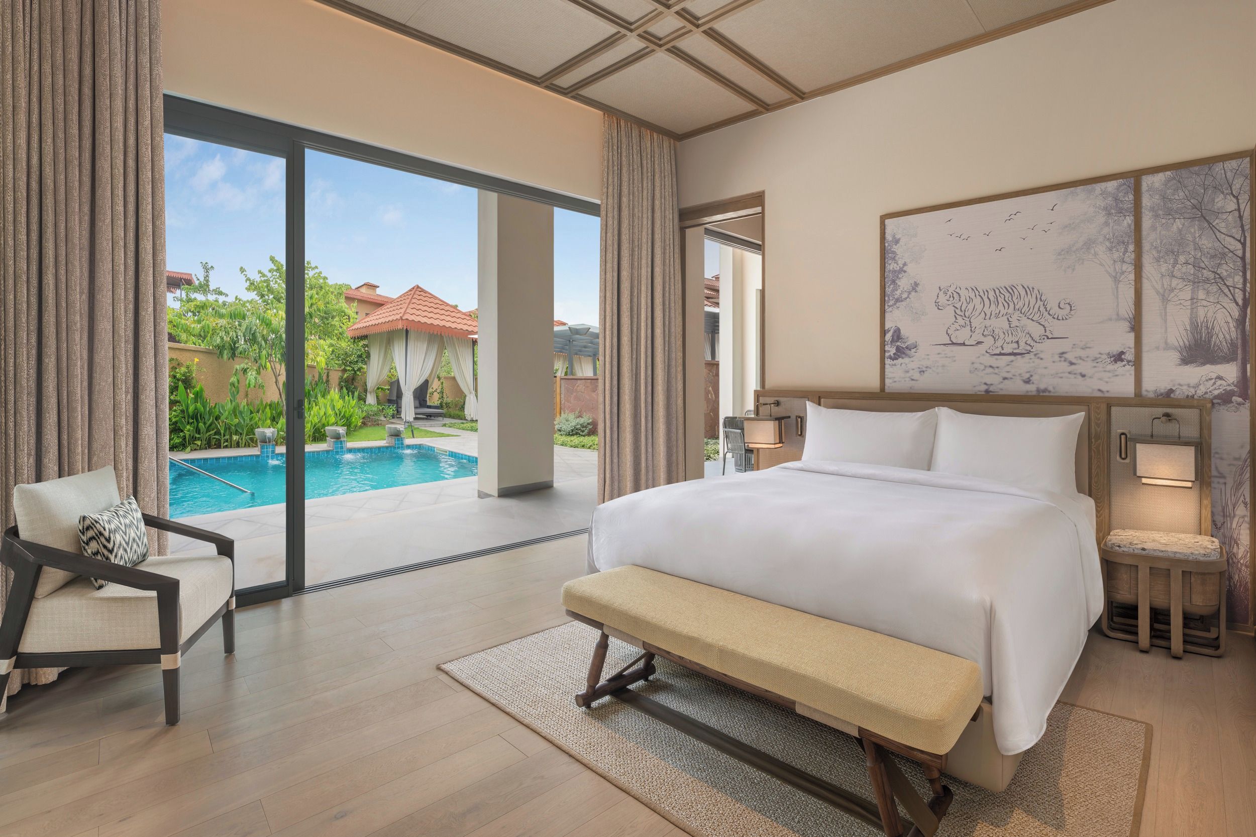 Habitación de hotel con una cama grande, un banco, una silla, vista a la piscina y un cuadro en la pared.