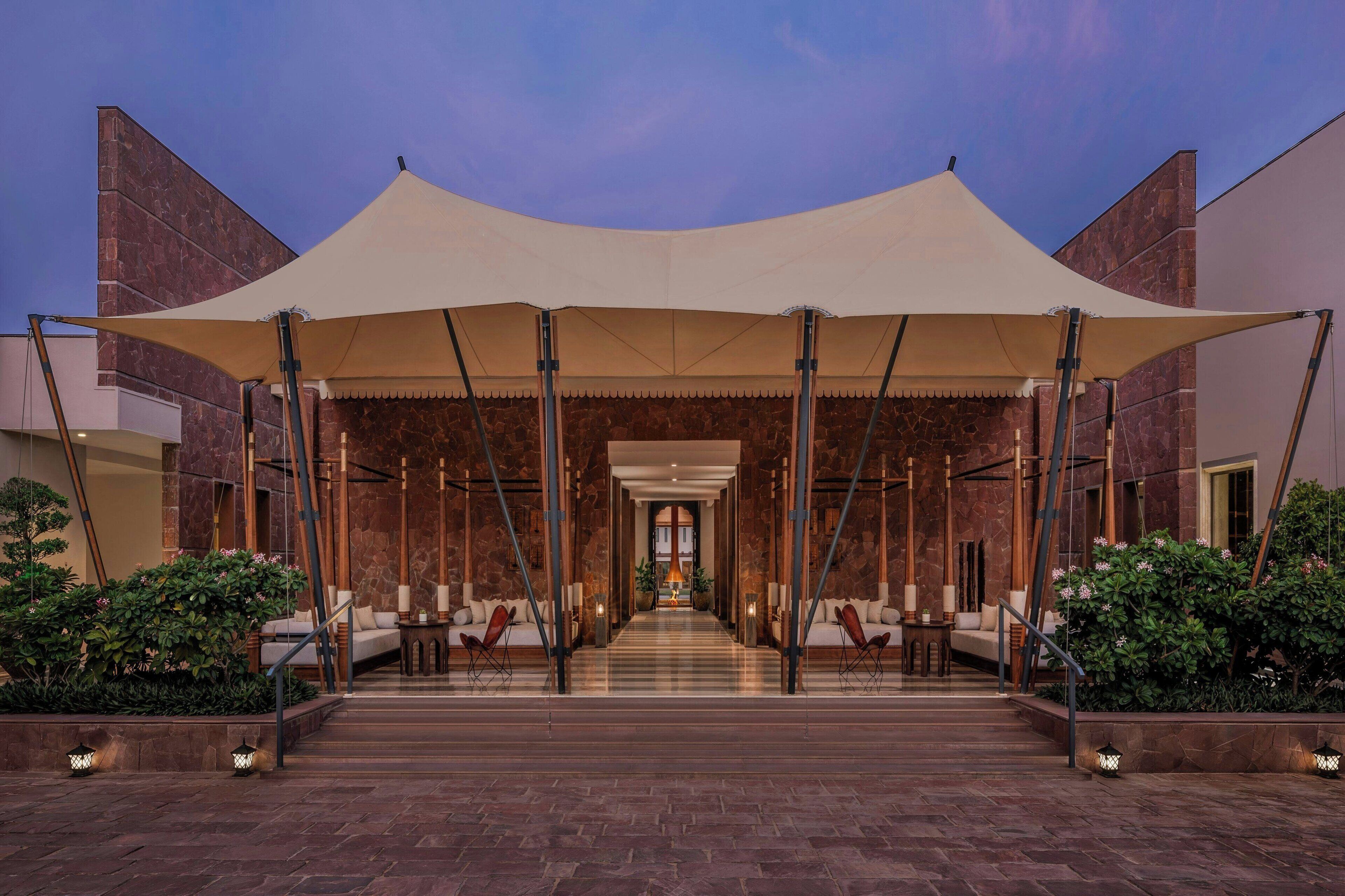 A hotel entrance with a covered walkway, stone walls, and seating areas.