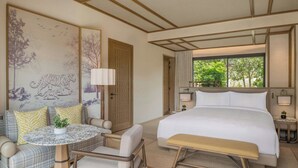 A hotel room with a bed, a seating area with a table and chairs, a large window, and artwork on the walls. - JW Marriott Ranthambore Resort & Spa (Sawai Madhopur)