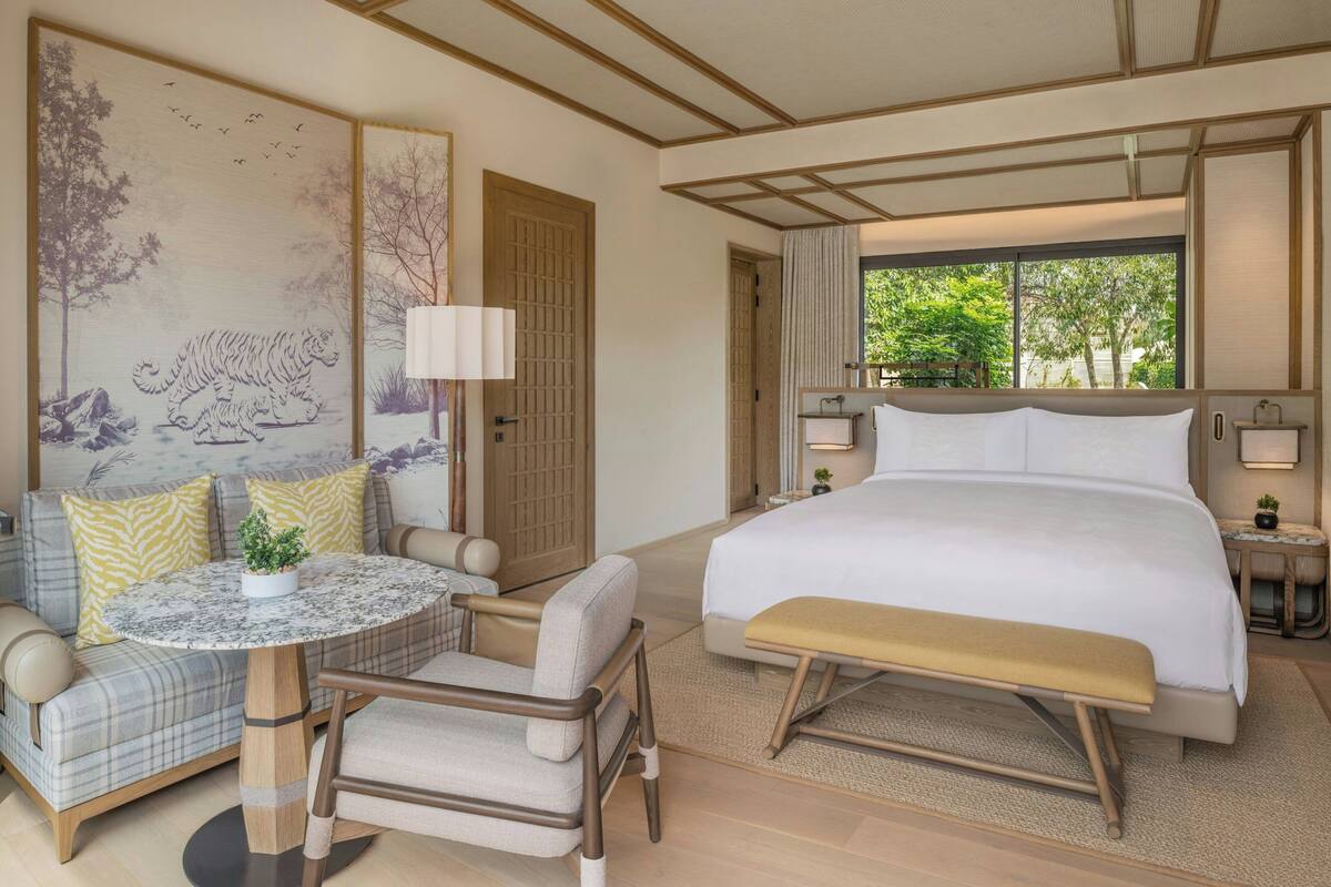 A hotel room with a bed, a seating area with a table and chairs, a large window, and artwork on the walls.